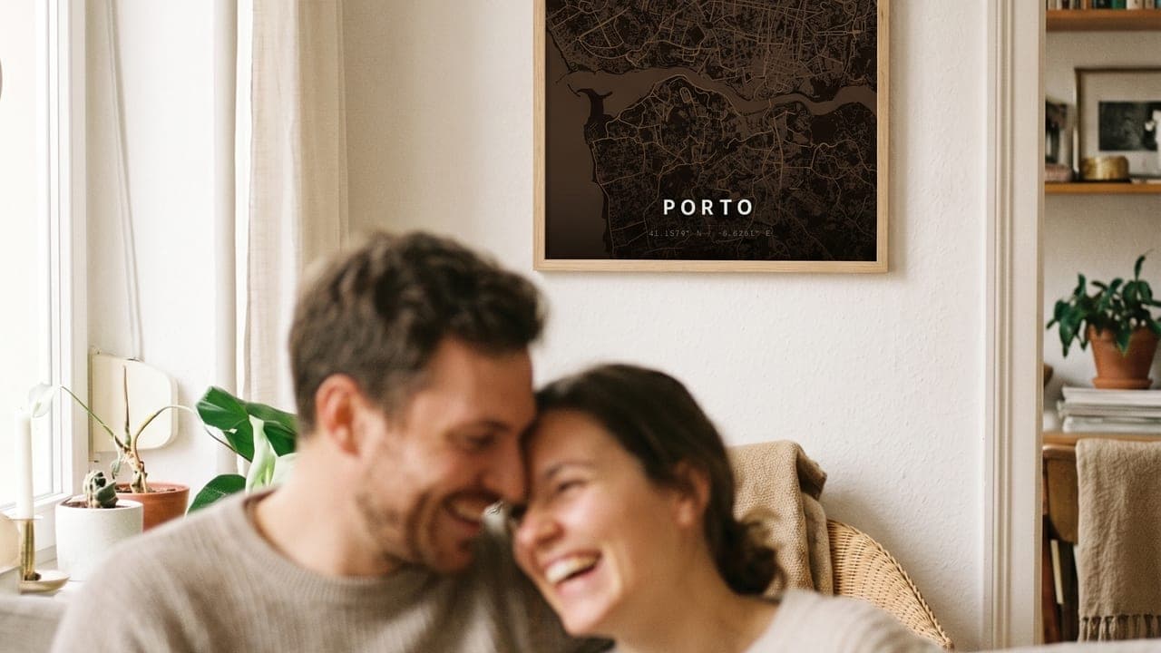 Couple laughing together on a sofa beneath a framed Porto map poster